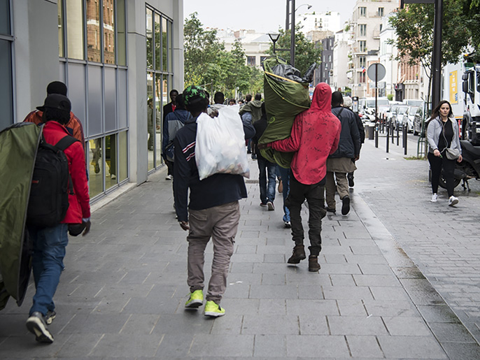 مهاجرون في طريقهم لنصب خيمهم في إحدى حدائق باريس (وكالة الأناضول)