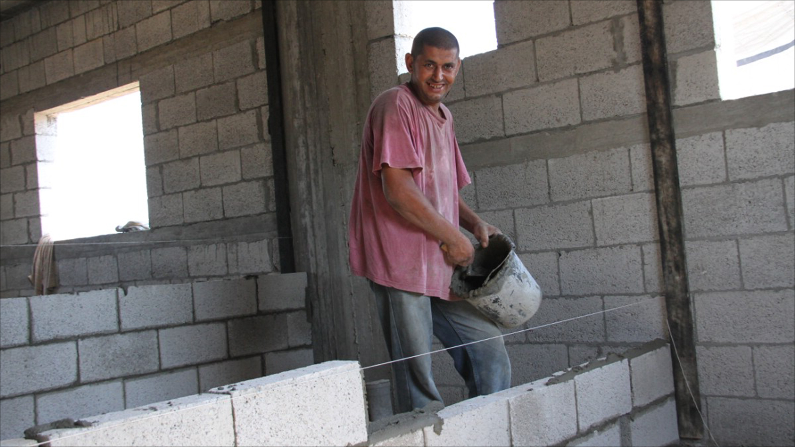 الخريج الجامعي محمد العماوي أثناء بناء حائط في منزل (الجزيرة)