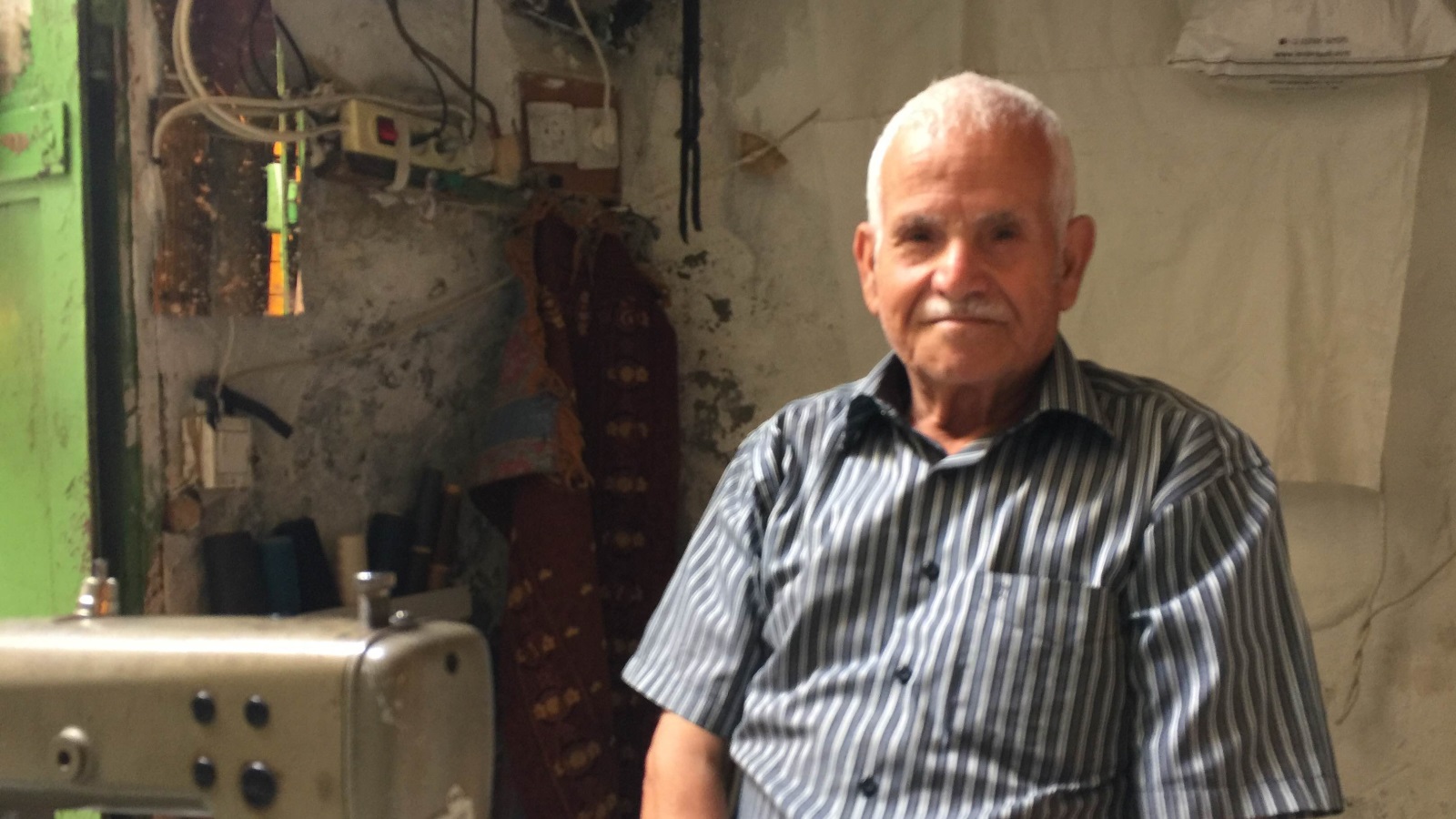 يملك الكركي ماكينة خياطة في محل صغير يملكه بسوق الباشورة منذ 58 عاما (الجزيرة نت)