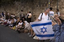 An Israeli woman uses her cellphone as a man holds an Israeli flag before a line of Israeli Arab women seated on the curb near the Jerusalem residence of Israeli Prime Minister Benjamin Netanyahu, during the conclusion of the Women Wage Peace march across Israel, 19 October 2016. About 1,000 women including many Israeli Arabs marched to demand Israel do more to promote peace.