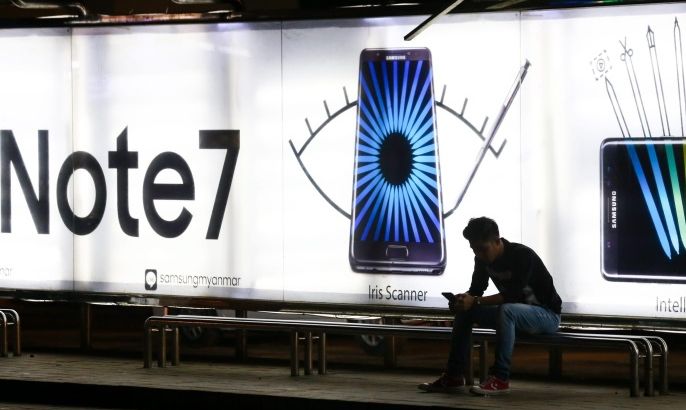 Myanmar man uses a mobile phone at a bus stop decorated with Samsung Galaxy Note 7 advertising in Yangon, Myanmar, 11 October 2016. Samsung has announced it is to permanently stop production of its high-end Galaxy Note 7 smartphones after reports of the phones catching fire.