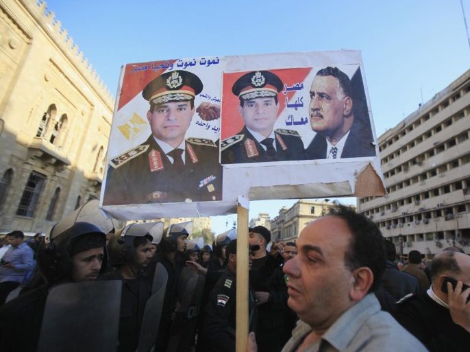 A supporter of Egypt's army chief General Abdel Fatah al-Sisi holds a poster of al-Sisi and former Egypt president Gamal Abdel Nasser, in front of the damaged buildings of the Cairo Security Directorate (R), which includes police and state security, and Museum of Islamic Art building, after a bomb attack in downtown Cairo, January 24, 2014. A suicide bomber in a car blew himself up in the parking lot of a top security compound in central Cairo on Friday, killing at least four people in one of the most high-profile attacks on the state in months, security sources said. The poster reads " We will die and Egypt will live. Egypt is with you." REUTERS/Amr Abdallah Dalsh (EGYPT - Tags: POLITICS CRIME LAW CIVIL UNREST)
