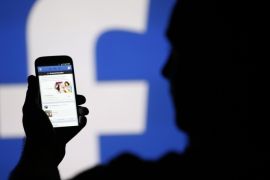 A man is silhouetted against a video screen with an Facebook logo as he poses with an Samsung S4 smartphone in this photo illustration taken in the central Bosnian town of Zenica, August 14, 2013. REUTERS/Dado Ruvic/File Photo