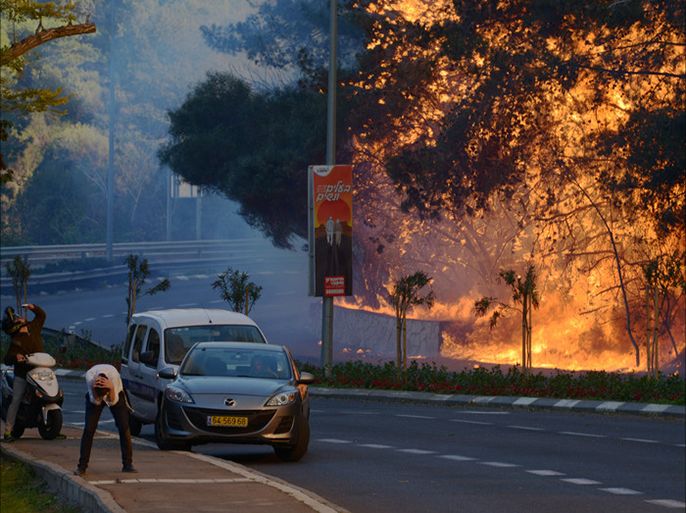 epa05645789 A man cover his head across the street from burning trees in a suburb of the coastal city of Haifa, north of Israel, 24 November 2016. The dry air and strong winds caused the fire transmission to different locations, Israeli police have opened an investigation into whether the fires that swept Israel is an active reaction, Israeli Police spokeswomen report. EPA/GIL ELIYAHU / JINIPIX ISRAEL OUT
