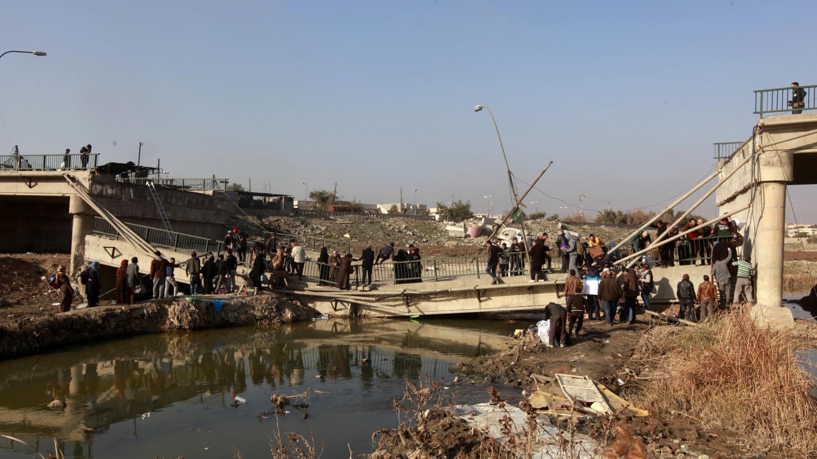 ‪مدنيون ينزحون عبر جسر مدمر من حي المثنى المقابل لمنطقة آثار نينوى في الموصل‬ (رويترز)