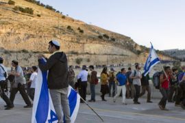 An Israeli adjusts his flag as others dance as they cross a bridge over the main Jerusalem to Jericho highway during a march from Ma'ale Adumim (behind) to the area called E1, east of Jerusalem, West Bank, 13 February 2014. Several thousands Israeli settlers and supporters marched from the sprawling Jewish settlement of Ma'ale Adumim to the E1 area in a show of support for expanding the Jewish settlement in the greater 'land of Israel.'