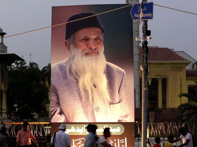 People pass next to portrait of Abdul Sattar Edhi the head and founder of The Edhi Foundation, the largest nonprofit social welfare program in Lahore, Pakistan, 09 July 2016. Abdul Sattar Edhi, died in Karachi on 08 July 2016 following Kidney problems at the age of 88.