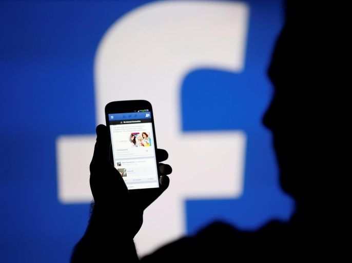 A man is silhouetted against a video screen with a Facebook logo as he poses with a Samsung S4 smartphone in this photo illustration taken in the central Bosnian town of Zenica, August 14, 2013. REUTERS/Dado Ruvic/File Photo