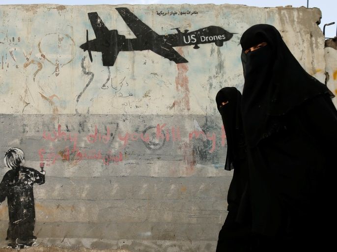 Women walk past a graffiti, denouncing strikes by U.S. drones in Yemen, painted on a wall in Sanaa, Yemen February 6, 2017. Picture taken February 6, 2017. REUTERS/Khaled Abdullah