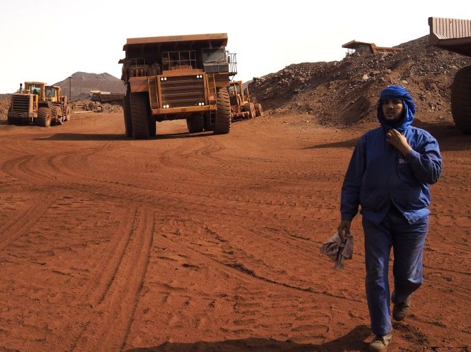 A SNIM truck driver walks in front of trucks at the TO-14 iron ore mine in Zouerate June 23, 2014. Mauritania's SNIM iron ore mining company aims to produce 13 million tonnes in 2014, around the same level as last year, the majority state-owned firm said. SNIM mines black iron ore in the northern town of Zouerate, a remote desert location which nevertheless attracts people from all over the country looking for work. SNIM employees proudly call their firm the lung of their nation's economy and the train that ferries the ore to the coast stretches some two kilometres, making it one of the world's longest. Picture taken June 23, 2014. REUTERS/Joe Penney (MAURITANIA - Tags: BUSINESS COMMODITIES ENVIRONMENT SOCIETY EMPLOYMENT)ATTENTION EDITORS: PICTURE 02 OF 33 FOR PACKAGE 'JOURNEY THROUGH MAURITANIA'TO FIND ALL IMAGES SEARCH 'PENNEY SNIM'
