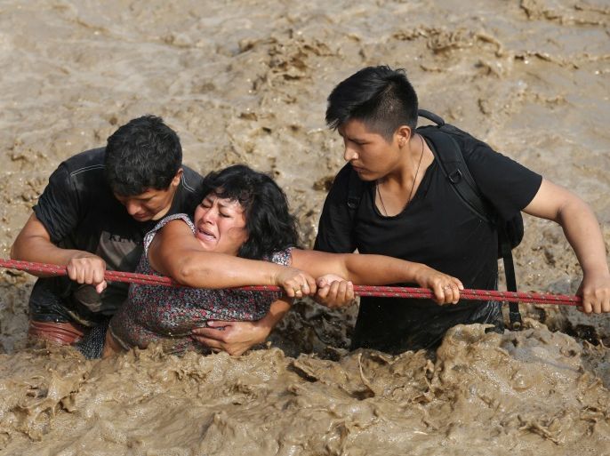 A woman is assisted while crossing a flooded street after the Huayco river overflooded its banks sending torrents of mud and water rushing through the streets in Huachipa, Peru, March 17, 2017. REUTERS/Guadalupe Pardo