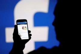 FILE PHOTO: A man is silhouetted against a video screen with a Facebook logo as he poses with a Samsung S4 smartphone in this photo illustration August 14, 2013. REUTERS/Dado Ruvic/File Photo