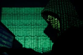 A hooded man holds a laptop computer as cyber code is projected on him in this illustration picture taken on May 13, 2017. REUTERS/Kacper Pempel/Illustration