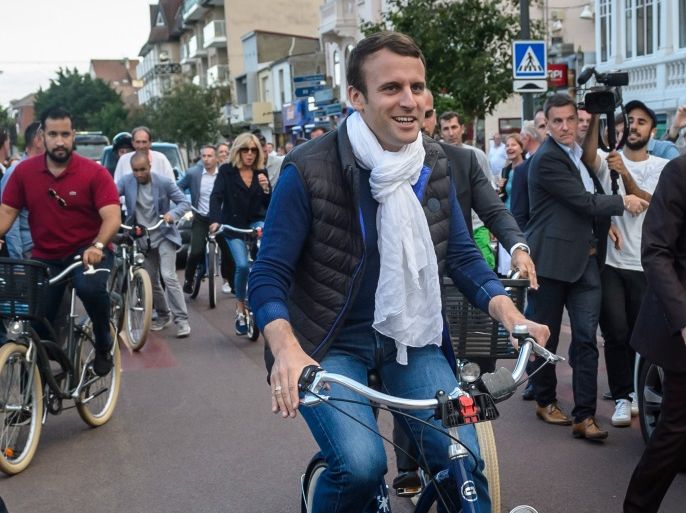 rench President Emmanuel Macron (C) and his wife Brigitte Trogneux (L) leave home on bicycles the day before the first round of the French legislatives