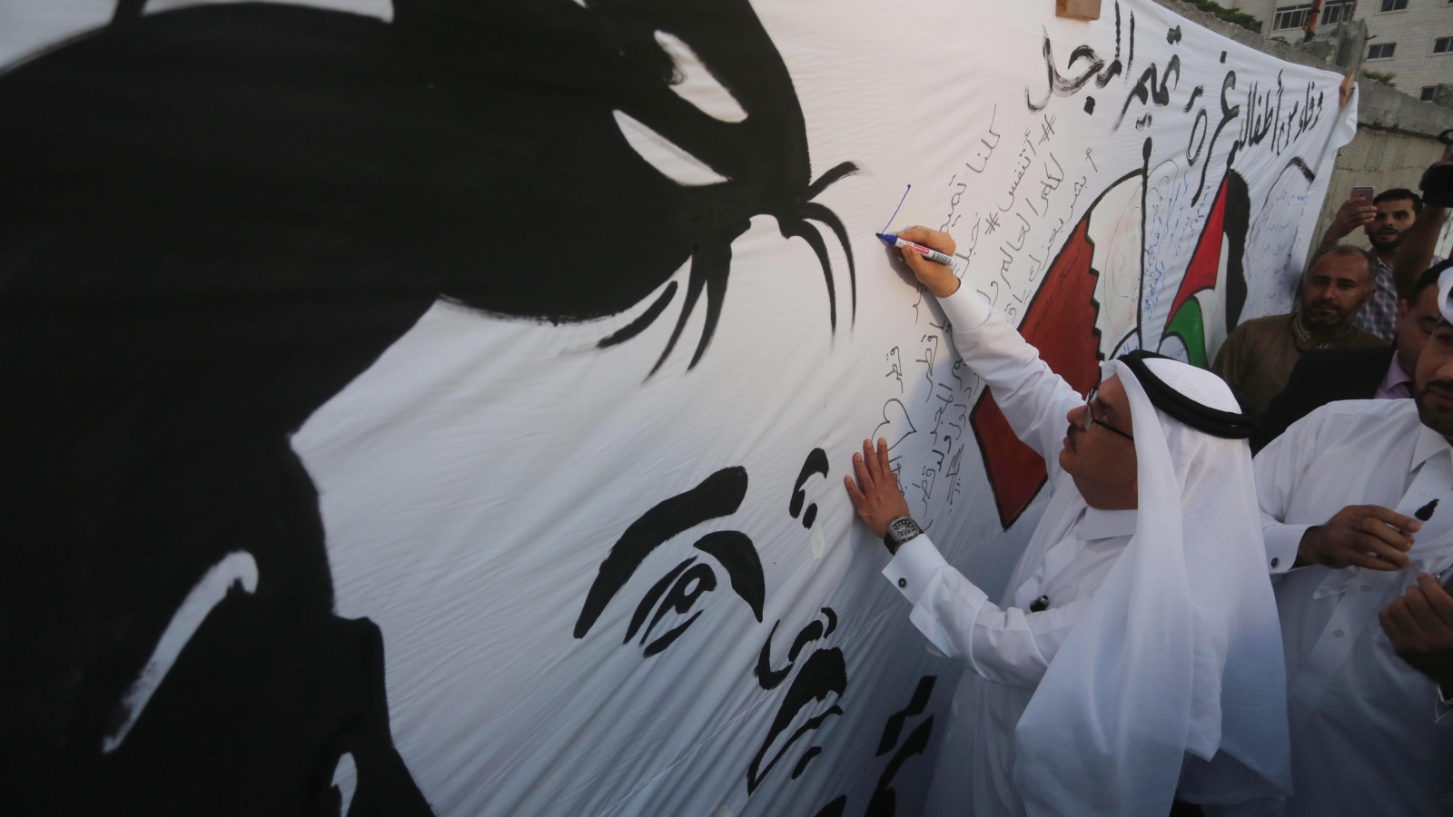 العمادي يوقع على الجدارية التي رسمها أطفال غزة (الجزيرة)