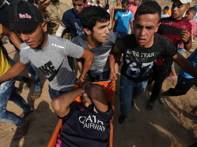 ‪‬ فلسطينيون ينقلون جريحا أصيب برصاص الاحتلال في مواجهات على الحدود مع قطاع غزة(رويترز)