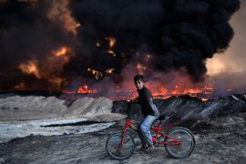 QAYYARAH, IRAQ - OCTOBER 21: A boy pauses on his bike as he passes an oil field that was set on fire by retreating ISIS fighters ahead of the Mosul offensive, on October 21, 2016 in Qayyarah, Iraq. Several hundred Iraqi families have been made to leave their homes for Mosul by Islamic State fighters as the UN warns they could be used as human shields. ISIS have attacked Kirkuk today as Kurdish and Iraqi forces, backed by a coalition including Britain and the U.S.A conti