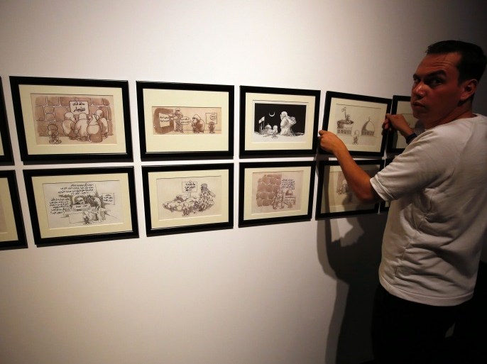 A man hangs cartoons by Palestinian caricaturist Naji al-Ali, who was assassinated in London 22 July 1987, during a media tour ahead of the 'Jerusalem Lives' exhibition at the Palestinian Museum on August 26, 2017, in the West Bank town of Birzeit, near Ramallah.The exhibition is scheduled to open on August 27 until December 15. / AFP PHOTO / ABBAS MOMANI / RESTRICTED TO EDITORIAL USE, MANDATORY CREDIT OF THE ARTIST, 'NAJI AL-ALI' TO ILLUSTRATE THE EVENT AS SPECIFIE