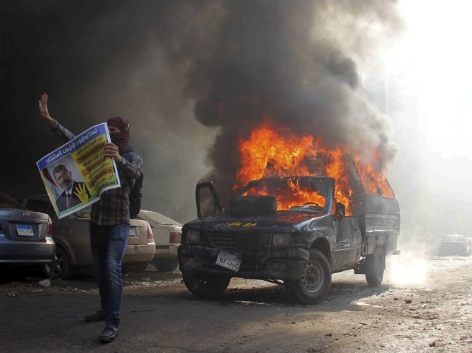 A supporter of the Muslim Brotherhood makes the Rabaa four-fingered gesture in front of a burning police vehicle in Cairo January 10, 2014. The four-fingered