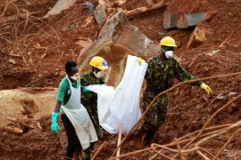 A volunteer and soldiers carry a victim across the mud, days following the partial collapse of a hillside that swept away hundreds of homes in a neighborhood of the capital Freetown on August 19, 2017.The death toll from the mudslide on August 14, 2017, and flooding that struck Sierra Leone's capital Freetown has reached 441, with around 600 others listed as missing the government said on August 19. / AFP PHOTO / SEYLLOU (Photo credit should read SEYLLOU/AFP/Getty Images)