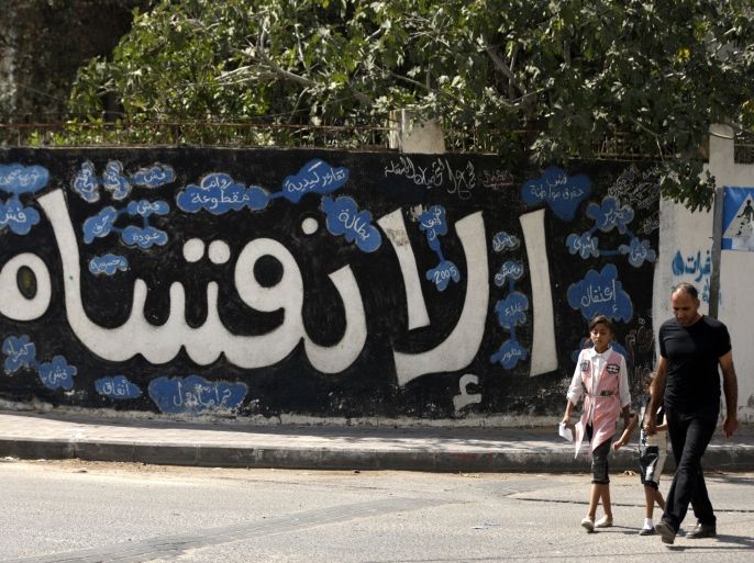 A Palestinian man and his daughter walk past a graffiti reading in Arabic ''Division'' in Gaza City, on September 17, 2017, after Hamas announced it had agreed to steps toward resolving a decade-long split with the Fatah movement and was ready to hold elections.Hamas said it had agreed to key demands made by Fatah: dissolving the so-called 'administrative committee', while saying it was ready for elections and negotiations toward a unity government. / AFP PHOTO /