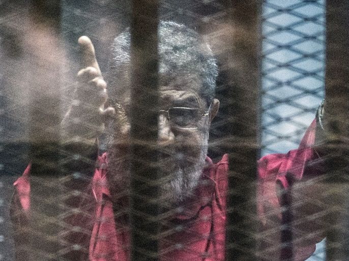 Egypt's ousted Islamist president Mohamed Morsi, wearing a red uniform, gestures from behind the bars during his trial in Cairo at the police academy in Cairo on April 23, 2016.An Egyptian court postponed its verdict and sentence in the trial of ousted Islamist president Mohamed Morsi, who is charged with spying for Qatar.The head judge of the criminal court said the verdict was postponed to 'May 7 to continue consultations,' in brief remarks aired on television. / A