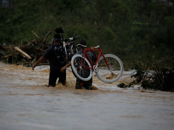 Men carrying bicycles wade through a flooded road after the area was hit by Hurricane Maria in Yauco, Puerto Rico September 21, 2017. REUTERS/Carlos Garcia Rawlins