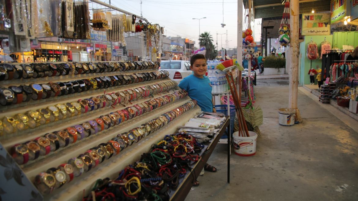 طفل يقف إلى جانب بسطية لبيع الإكسسوارات في إحدى الأسواق