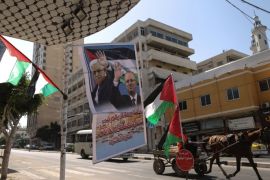 A Palestinian man rides a horse cart past national flags and a poster bearing the portraits Palestinian prime minister Rami Hamdallah and Palestinian leader Mahmud Abbas displayed outside a shop in Gaza city on October 1, 2017. / AFP PHOTO / MAHMUD HAMS (Photo credit should read MAHMUD HAMS/AFP/Getty Images)