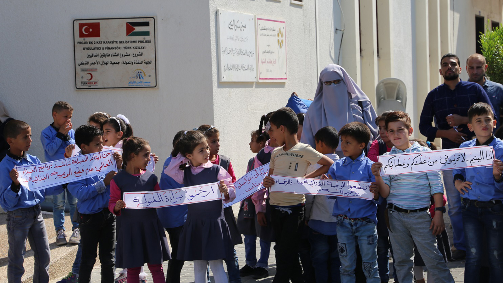 أطفال يرفعون لافتات طلبا لعدم قطع المساعدات الغذائية (الجزيرة)