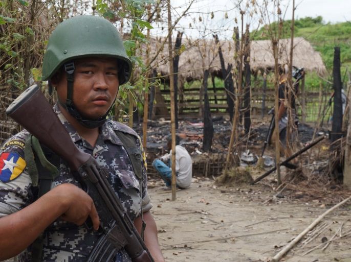 A Myanmar border guard police officer stands guard in front of the remains of a house burned down in a clash between suspected militants and security forces in Tin May village, Buthidaung township, northern Rakhine state, Myanmar July 14, 2017. Picture taken July 14, 2017. REUTERS/Simon Lewis
