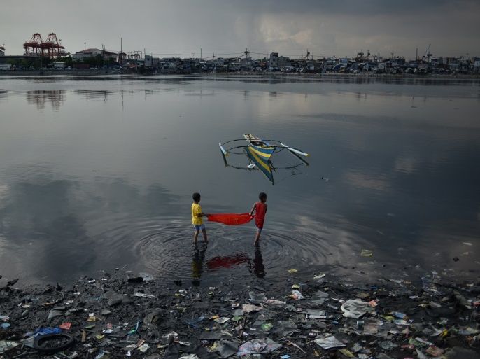 MANILA, PHILIPPINES - APRIL 25, 2017: Children trying to catch small fish with a sheet of plastic near their hose in a community near Manila bay on April 25, 2017 in Manila, Philippines. Metro Manila has been facing an increasing amount of floods due to overuse of groundwater causing the city to sink, as well as rapid rise in sea levels which has been over double the global average. The Philippines has been among the top five countries vulnerable to climate change over