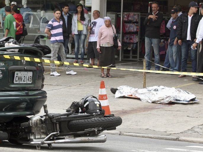 The body of a motorcycle courier lies on the street as pedestrians observe the aftermath an accident in Sao Paulo, November 13, 2012. Dying at the rate of three per day, according to official statistics, Sao Paulo's approximately 200,000 registered motorcycle couriers, nicknamed either motoboys or mad dogs, are the terror of drivers. Motoboys in the city bully drivers into giving them the right of way as they race along the corridors formed between the rows of vehicles stuck in heavy traffic, making them their exclusive high speed corridors. Picture taken November 13, 2012. REUTERS/Paulo Whitaker (BRAZIL - Tags: SOCIETY TRANSPORT)