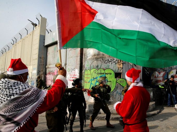 Palestinians dressed as Santa Claus stand in front of Israeli troops during a protest in the West Bank city of Bethlehem, December 23, 2017. REUTERS/Ammar Awad