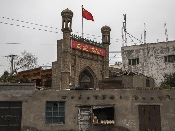KASHGAR, CHINA - JUNE 28: A Chinese flag flies over a local mosque recently closed by authorities as an ethnic Uyghur woman sells bread at her bakery on June 28, 2017 in the old town of Kashgar, in the far western Xinjiang province, China. Kashgar has long been considered the cultural heart of Xinjiang for the province's nearly 10 million Muslim Uyghurs. At an historic crossroads linking China to Asia, the Middle East, and Europe, the city has changed under Chinese r