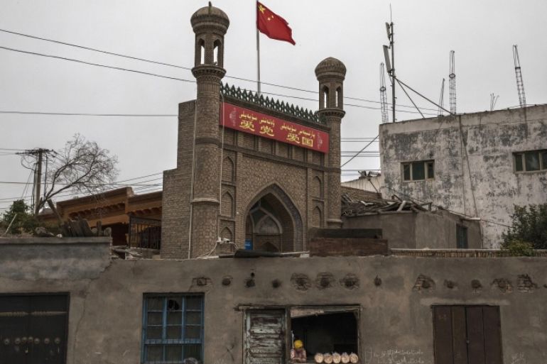 KASHGAR, CHINA - JUNE 28: A Chinese flag flies over a local mosque recently closed by authorities as an ethnic Uyghur woman sells bread at her bakery on June 28, 2017 in the old town of Kashgar, in the far western Xinjiang province, China. Kashgar has long been considered the cultural heart of Xinjiang for the province's nearly 10 million Muslim Uyghurs. At an historic crossroads linking China to Asia, the Middle East, and Europe, the city has changed under Chinese r