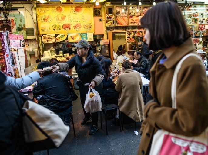 TOKYO, JAPAN - JANUARY 04: A waitress passes food to a colleague at a street food stall in Ameya Yokocho market on January 4, 2018 in Tokyo, Japan. Ameya Yokocho, claimed to be Tokyo's last remaining open air market, started out as a black market after WWII when American goods were sold there. It now has around 500 shops along a long, narrow lane and is visited by tens of thousands of people daily. (Photo by Carl Court/Getty Images)