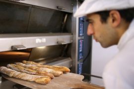 Baker Sylvain Cabane takes out of the oven a tray of baguettes at the bakery