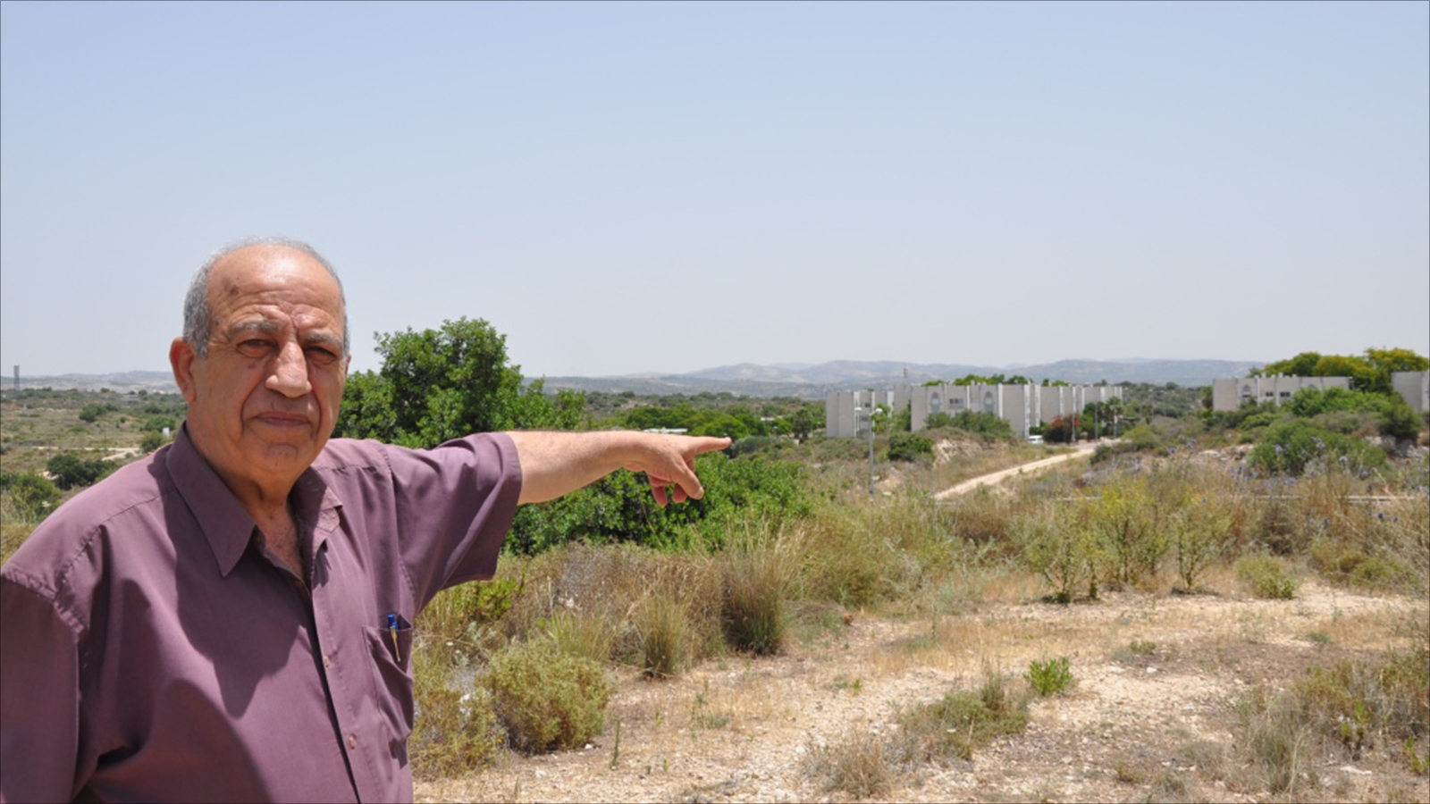 ‪أحمد ملحم شاهد على أحداث يوم الأرض في الطيبة يشير إلى مستوطنة حريش المقامة على أراض للفلسطينيين على جانبي الخط الأخضر‬ (الجزيرة)