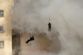 Palestinian members of al-Qassam Brigades, the armed wing of the Hamas movement, descend while being harnessed to zip lines as smoke engulfs a building during a military parade marking the 27th anniversary of Hamas' founding, in Gaza City December 14, 2014. REUTERS/Suhaib Salem (GAZA - Tags: POLITICS MILITARY ANNIVERSARY)