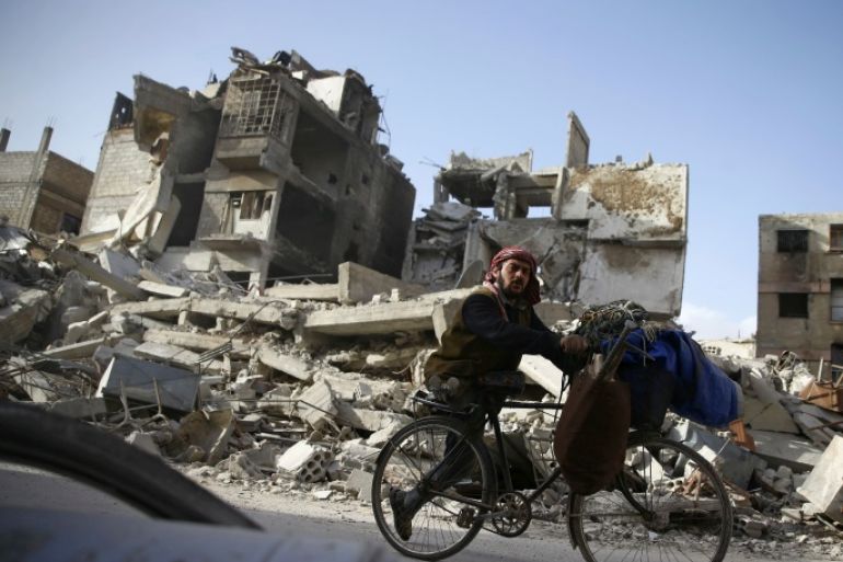 A handicapped man rides a bicycle past damaged buildings in the besieged town of Douma in eastern Ghouta in Damascus, Syria, March 1, 2018. REUTERS/Bassam Khabieh
