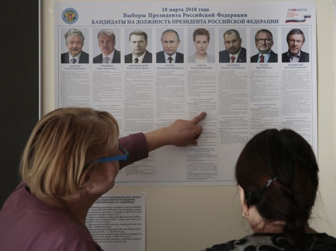 Women stand in front of a broadsheet with information about the candidates during preparations for the upcoming presidential election at a polling station in St. Petersburg, Russia March 17, 2018. REUTERS/Anton Vaganov