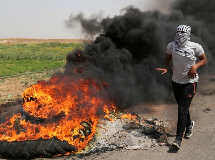 A Palestinian runs next to burning tyres during clashes along the Israel border with Gaza ahead of a protest in a tent city, demanding to return to their homeland, in the southern Gaza Strip March 29, 2018. REUTERS/Ibraheem Abu Mustafa