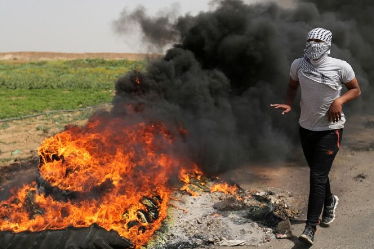 A Palestinian runs next to burning tyres during clashes along the Israel border with Gaza ahead of a protest in a tent city, demanding to return to their homeland, in the southern Gaza Strip March 29, 2018. REUTERS/Ibraheem Abu Mustafa