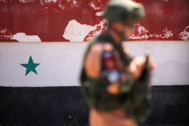 A Russian soldier stands guard near a Syrian national flag drawn on the wall as rebel fighters and their families evacuate the besieged Waer district in the central Syrian city of Homs, after an agreement reached between rebels and Syria's army, Syria May 21, 2017. REUTERS/Omar Sanadiki