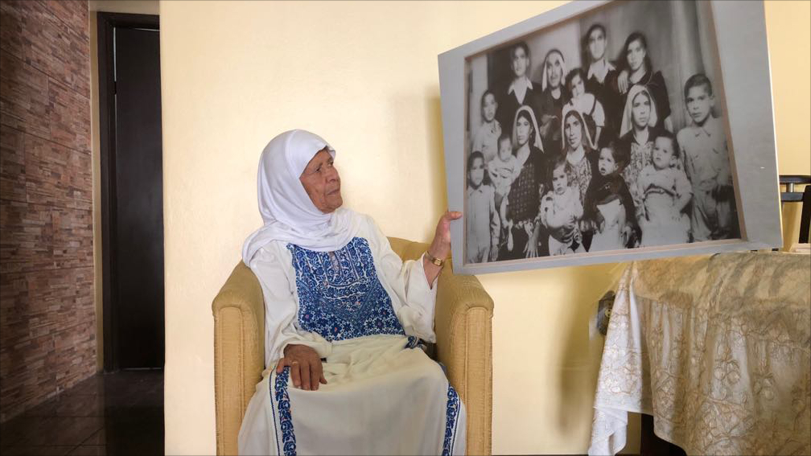  نسيمة جندي مع صورة عائلتها في فلسطين عام 1956 والتي تحتفظ بها منذ ذلك العام (الجزيرة)