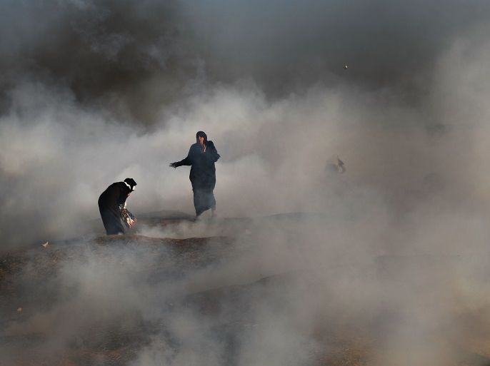 GAZA CITY, GAZA - MAY 15: Two women struggle in a cloud of tear gas at the border fence with Israel on May 15, 2018 in Gaza City, Gaza. Israeli soldiers killed over 50 Palestinians and wounded over a thousand as demonstrations on the Gaza-Israel border coincided with the controversial opening of the U.S. Embassy in Jerusalem yesterday. This marks the deadliest day of violence in Gaza since 2014. Gaza's Hamas rulers have vowed that the marches will continue until the d