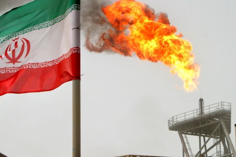 A gas flare on an oil production platform in the Soroush oil fields is seen alongside an Iranian flag in the Persian Gulf, Iran, July 25, 2005. To match Exclusive OPEC-OIL/ REUTERS/Raheb Homavandi/File Photo