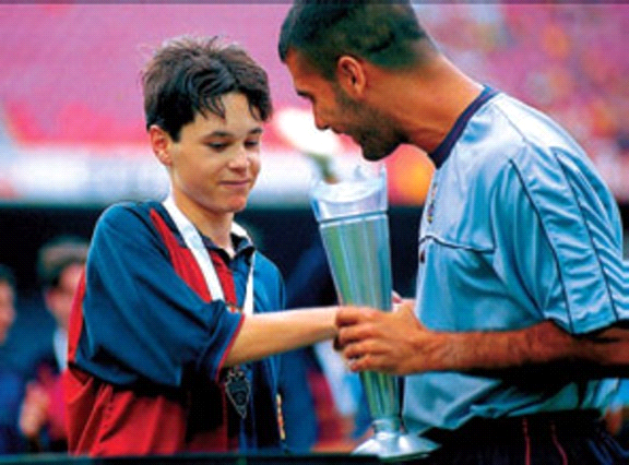 (بيب غوارديولا -لاعب وسط برشلونة آنذاك- يُسلم كأس البطولة للناشئ الخجول إنييستا ابن الخامسة عشر)