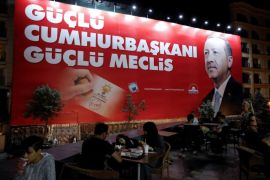 People sit in a restaurant terrace as a pre-election poster depicting Turkish President Tayyip Erdogan reads